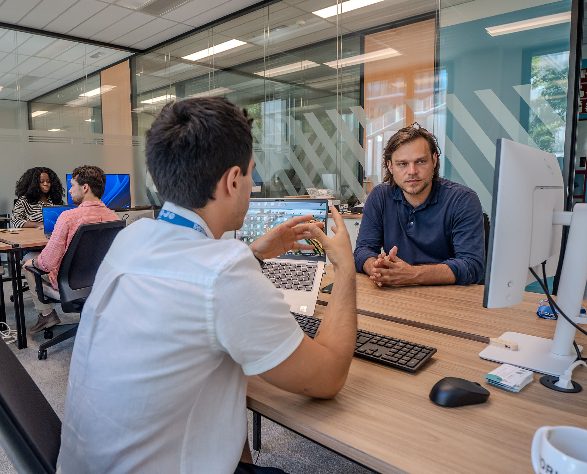 2 hommes dans un bureau discutent face à un ordinateur.